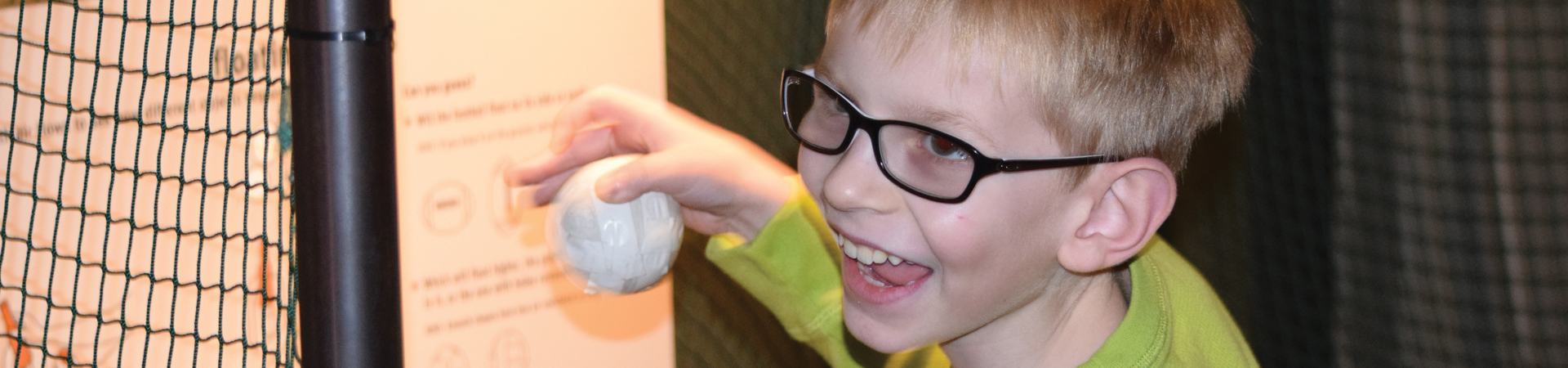 A young blind boy smiles as he plays with a ball.