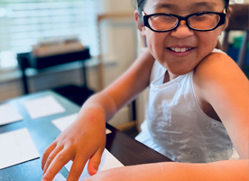 A young blind girl smiles while reading a Braille page.
